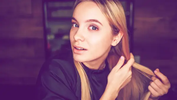 Junge Frau mit blonden Haaren, die sich die Haare für die Olaplex No. 0 Anwendung zurechtmacht.