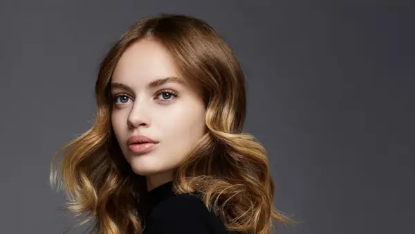 Porträt einer jungen Frau mit welligem, braunem Haar, das mit Balayage-Technik aufgehellt wurde.