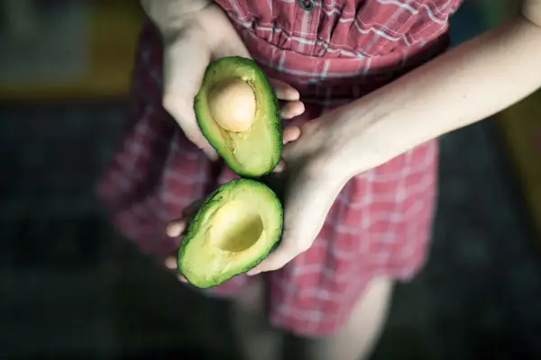 Hände halten eine aufgeschnittene Avocado, bereit für eine pflegende Avocado-Maske für die Haare.