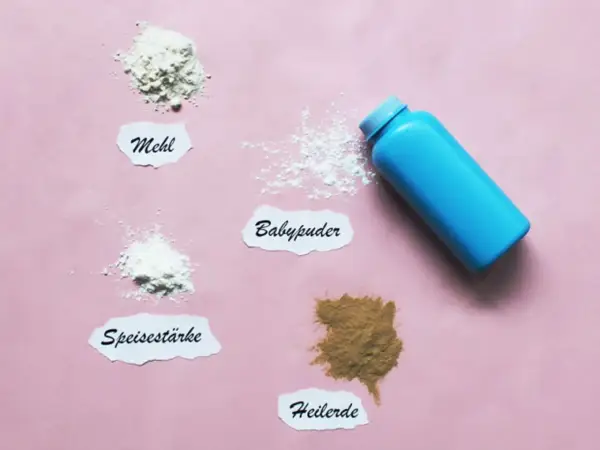 Blauer Behälter mit Babypuder, daneben Häufchen von Mehl, Speisestärke und Heilerde. Babypuder als trockenshampoo für schnelle Hilfe.