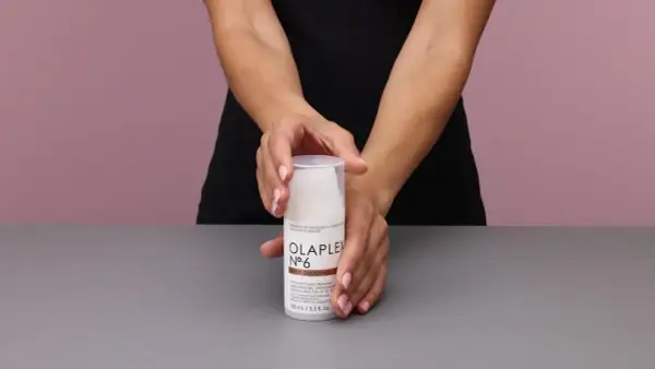 Hände halten eine Flasche Olaplex Nr. 6 Bond Smoother, ein Leave-in Styling Treatment für Feuchtigkeit und Stärke.