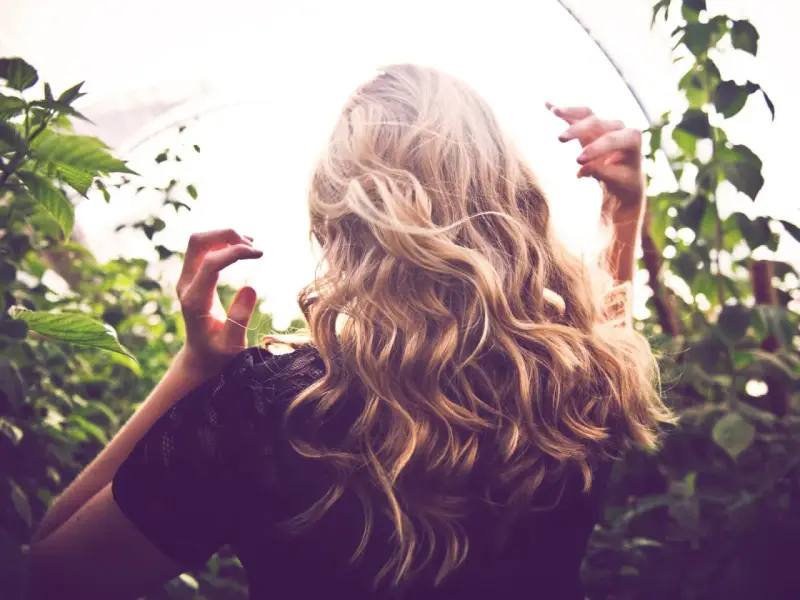 Frau mit welligem Haar, das einen subtilen Reverse Balayage-Effekt zeigt. Vorher-Nachher-Verwandlung für einen natürlichen Look.